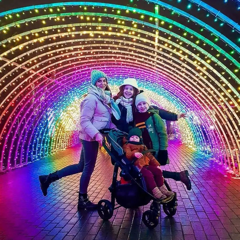 Mamă cu copii și cărucior într-un tunel luminos în culorile curcubeului
